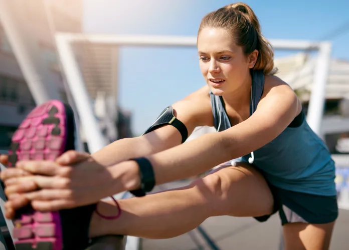 Woman, stretching legs and bridge in city, morning and warm up with fitness, health and wellness in sunshine. Runner, girl and person with workout, muscle and ready to start exercise in Germany Mujer runner realiza estiramientos